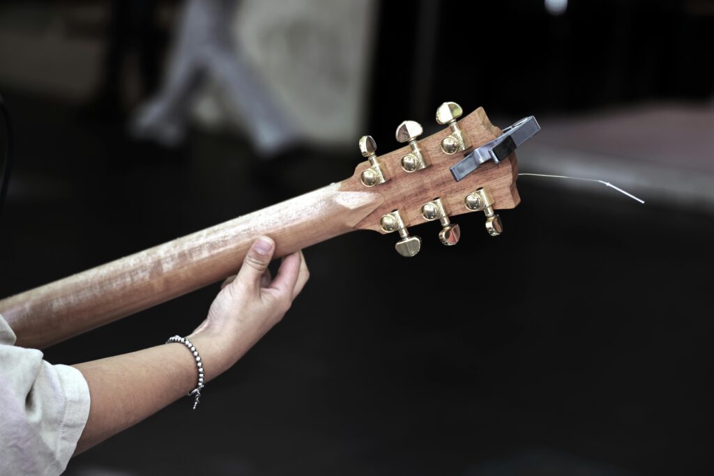 A person tunes an acoustic guitar outdoors, focusing on the headstock and tuning pegs.